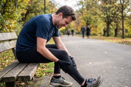 Coureur assis sur un banc massant son tibia douloureux pendant une sortie running en parc urbain