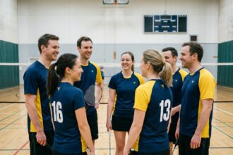 Équipe de badminton adulte en maillots personnalisés bleu marine et jaune posant sur un terrain de gymnase